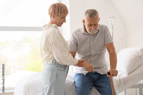 Mature woman helping her husband with stick in clinic