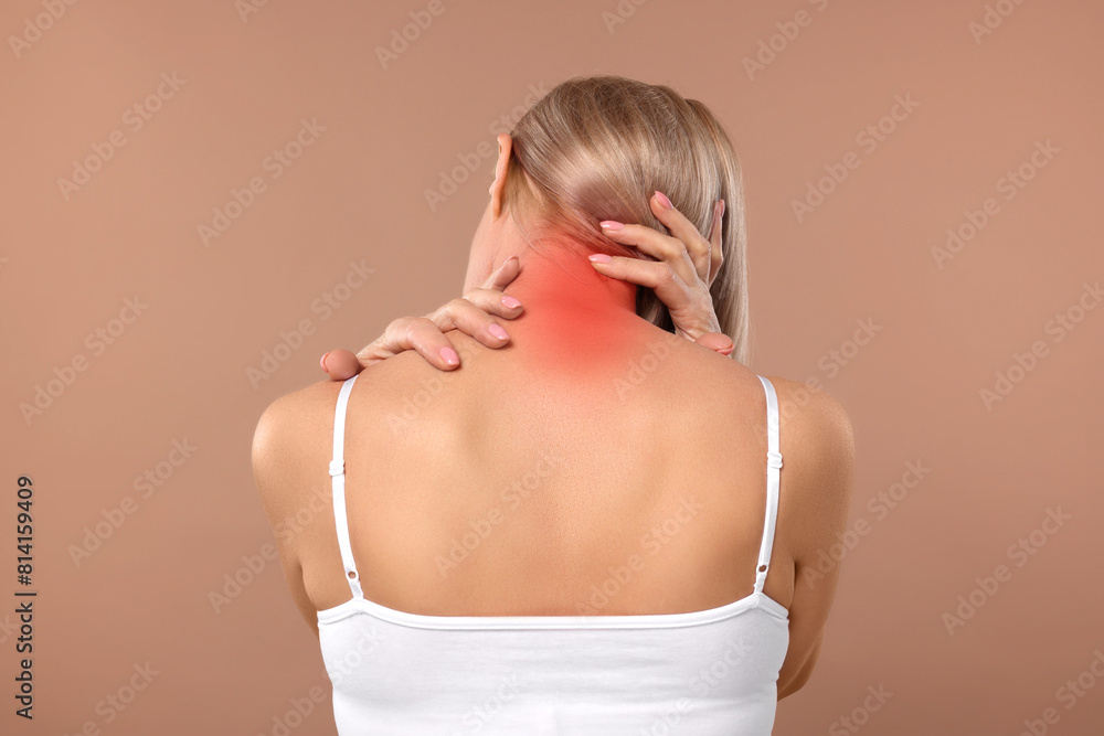 Woman suffering from neck pain on dark beige background, back view Woman suffering from neck pain on dark beige background, back view