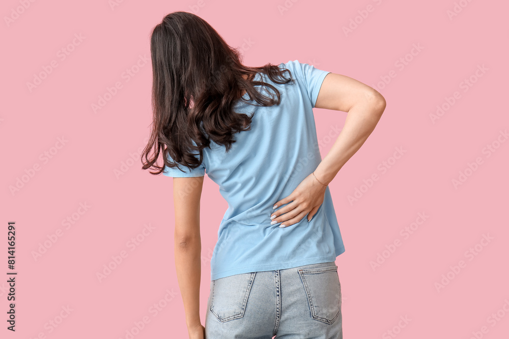 Beautiful young woman suffering from back pain on pink background Beautiful young woman suffering from back pain on pink background