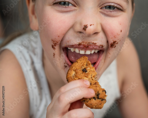 A cute little girl smeared in chocolate eats cookies while lying on the sofa.
