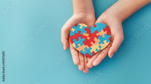 Conceito do dia mundial de conscientização do autismo. Mãos de adultos e crianças segurando um coração de quebra-cabeça sobre fundo azul claro. Vista do topo