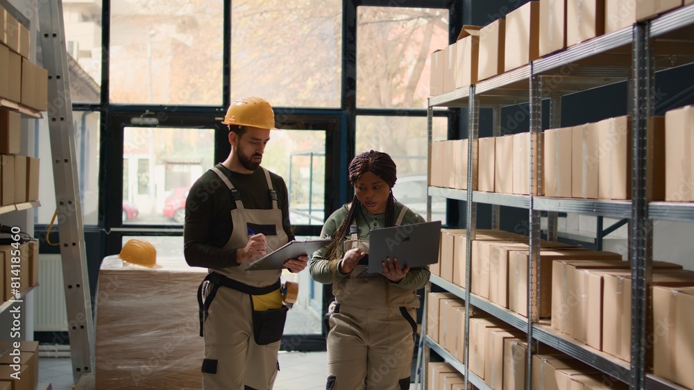 Warehouse chief logistics officer and intern inputing updated products info on online shopping website, walking through storeroom aisles inspecting labels on wares sitting on shelves Warehouse chief logistics officer and intern inputing updated products info on online shopping website, walking through storeroom aisles inspecting labels on wares sitting on shelves