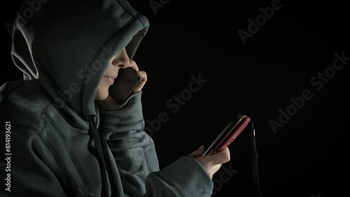 Female hacker is using a phone. A view of female hacker tall on phone and typing a message on the black background. A concept of cyber program on smartphone.