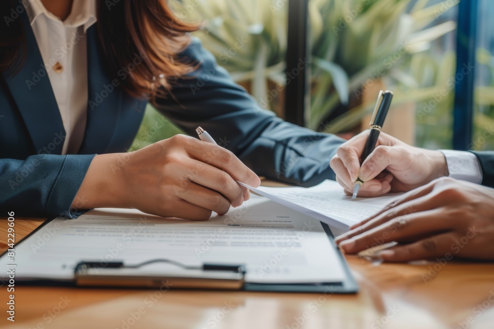 Close up of hands with pen and documents on a desk, a woman in a suit showing a document to a customer during a contract meeting. Close up of hands with pen and documents on a desk, a woman in a suit showing a document to a customer during a contract meeting.