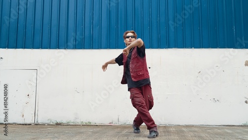 Handsome street dancer practicing break dancing at white back ground. Sport man wearing hip hop style while moving footsteps to music at street with blue background. Outdoor sport 2024. Endeavor.