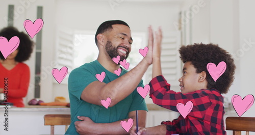 Image of social media heart icons over smiling biracial man and son high fiving