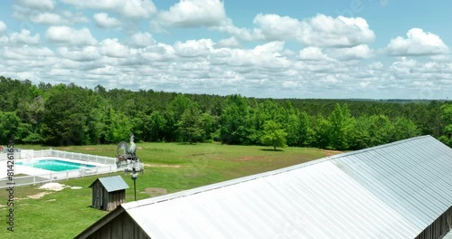Slow motion shot of a rooster wind vane on top of a tin roof barn with a house and swimming pool in the background