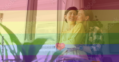 Image of heart emojis and rainbow flag over caucasian female couple embracing