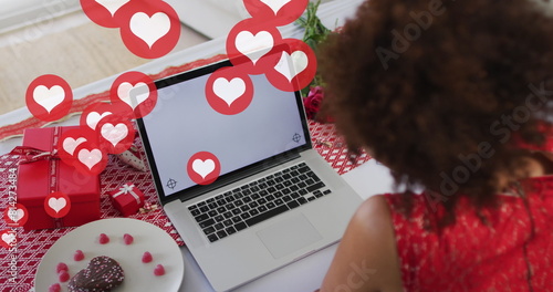 Image of heart icons over african american woman using laptop with copy space, slow motion