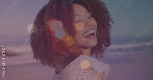 Image of lens flares over portrait of biracial young woman with afro hair laughing at beach