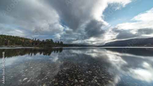 Clouds fla fast and are reflected in the mirrorlike surface of the shallow lake with clear transparent waters. A timelapse video. photo