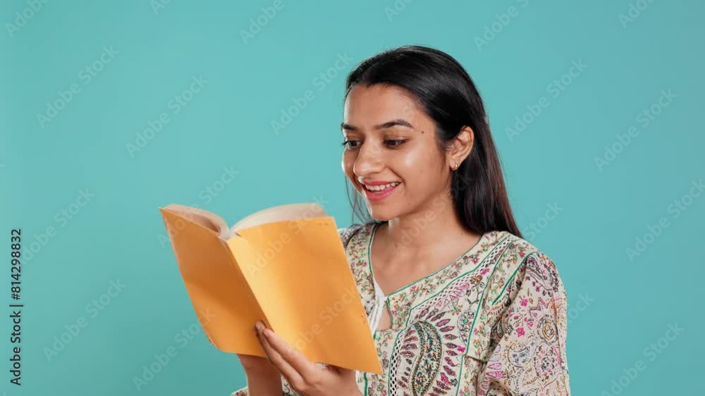 Cheerful woman smiling while enjoying reading activity, holding book, isolated over studio background. Radiant person pleased with entertaining novel, enjoying leisure time, camera B Cheerful woman smiling while enjoying reading activity, holding book, isolated over studio background. Radiant person pleased with entertaining novel, enjoying leisure time, camera B
