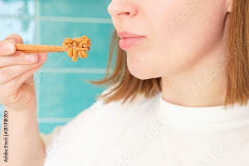 Young woman eating natto beans with wooden chopsticks, side view.