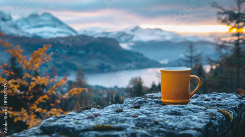 A tranquil scene depicting a yellow coffee mug on a rock, overlooking a misty mountain landscape at sunrise.