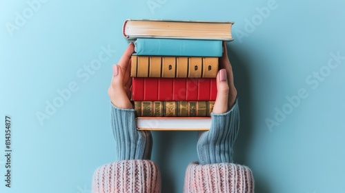 Woman hands holding pile of books over light blue background. Education, library, science, knowledge, studies, book swap, hobby, relax time photo