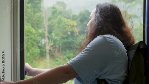 Passenger looking at view from open door. Woman with backpack traveling in train. She is exploring during vacation.