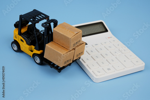 White calculator and yellow forklift truck carrying carton boxes on blue background. Price of shipping concept.