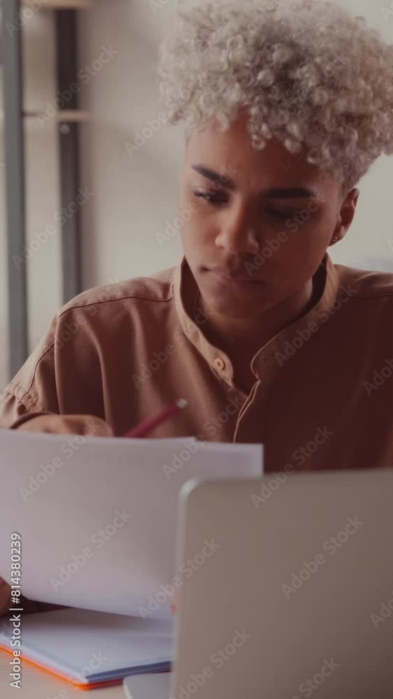 Young focused African American business woman dealing with paperwork and bureaucracy going through documents and checking reports of subordinates dressed in casual clothes sits at desk in office. Young focused African American business woman dealing with paperwork and bureaucracy going through documents and checking reports of subordinates dressed in casual clothes sits at desk in office.