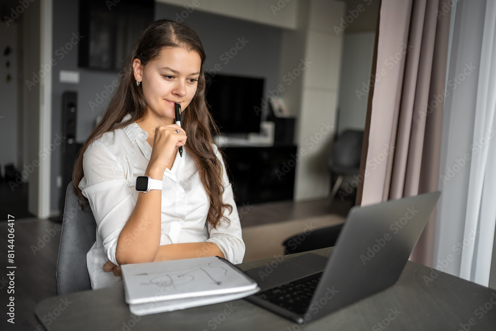 Young woman using laptop in home workplace, writing notes, female student learning and watching online webinar or listening audio course, e-learning education concept. Young woman using laptop in home workplace, writing notes, female student learning and watching online webinar or listening audio course, e-learning education concept.
