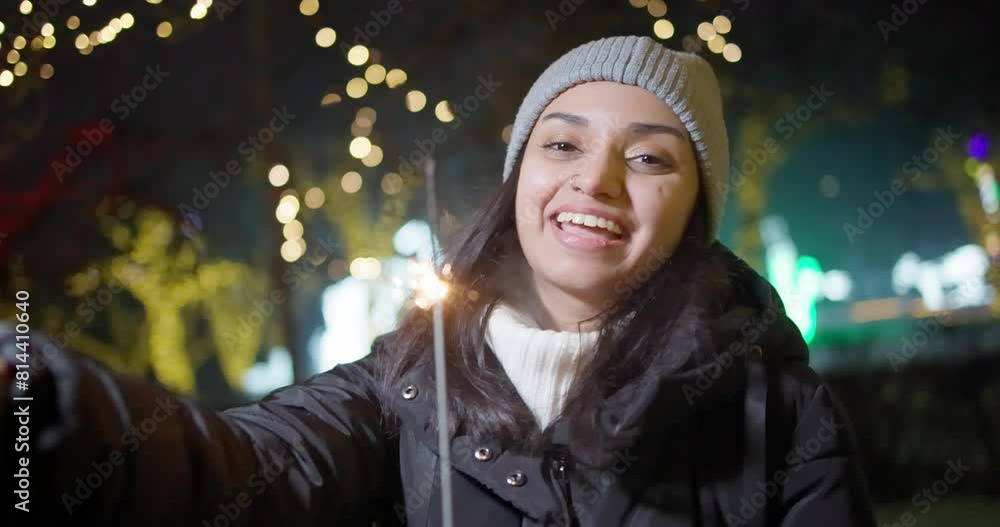 Young Indian Woman making video call holding sparkler standing on lights and garlands background, New Year and Christmas concept Young Indian Woman making video call holding sparkler standing on lights and garlands background, New Year and Christmas concept