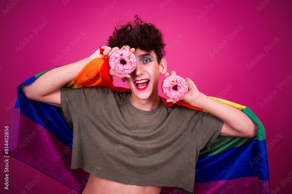 A funny guy dressed as a drag queen and eating pink donuts. Pink background. A funny guy dressed as a drag queen and eating pink donuts. Pink background.