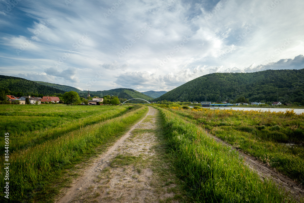Panorama of the village of Porąbka seen from the walking path along Lake Czanieckie. Spring in the Beskid Mały Mountains. The bridge in the distance. A fragment of the blue tourist trail