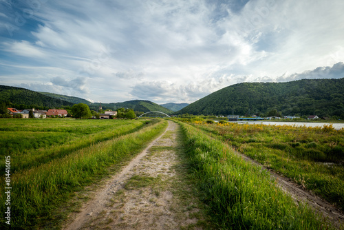 Panorama of the village of Porąbka seen from the walking path along Lake Czanieckie. Spring in the Beskid Mały Mountains. The bridge in the distance. A fragment of the blue tourist trail