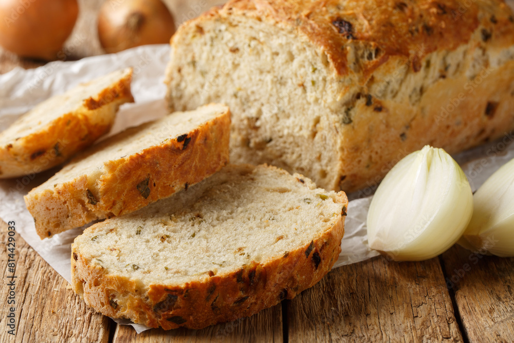 Freshly baked onion bread sliced loaf close-up on parchment on a wooden table. Horizontal Freshly baked onion bread sliced loaf close-up on parchment on a wooden table. Horizontal