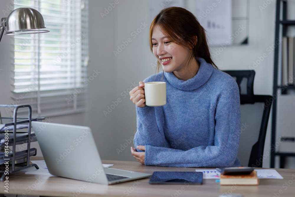 Freelancer asian woman working from home and using laptop sitting in living room with cup of hot coffee enjoying Freelancer asian woman working from home and using laptop sitting in living room with cup of hot coffee enjoying