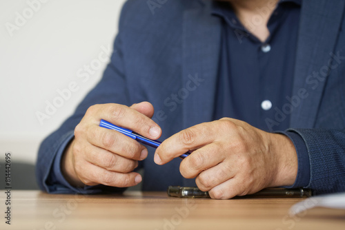 Elegant adult man holding a fountain pen in his hand while sitting at a table next to a smartphone and documents. Business meeting or negotiations. No face. Photo. Selective focus
