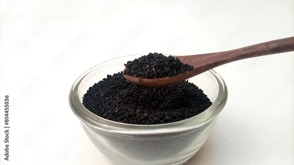 Spoon out of Black cumin seeds or black caraway seeds from the glass bowl with a wooden spoon, herbs and spices Spoon out of Black cumin seeds or black caraway seeds from the glass bowl with a wooden spoon, herbs and spices