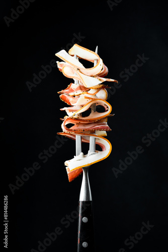 Slices of smoked bacon on a metal fork. On a black background, close-up. photo