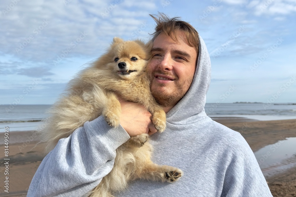 Happy young man walking with his Pomeranian spitz dog, hold puppy on hands on the beach at summer sunny day. Happy young man walking with his Pomeranian spitz dog, hold puppy on hands on the beach at summer sunny day.