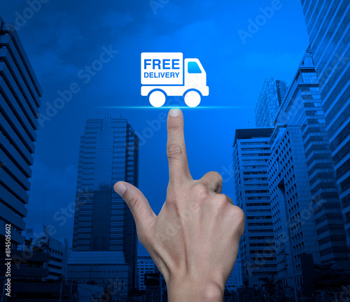 Hand pressing free delivery truck flat icon over modern city tower and skyscraper, Business transportation service concept