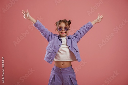 Smiling, with hands up and on the sides. Cute little girl is against pink background © standret