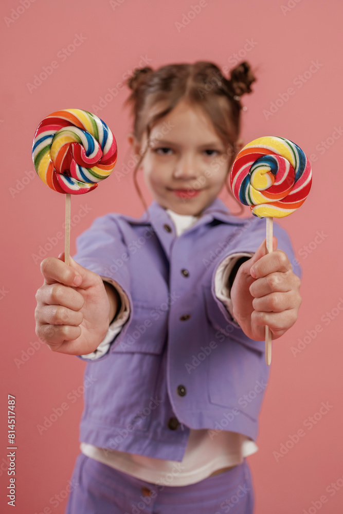 Posing and showing two candies. Cute little girl is against pink background