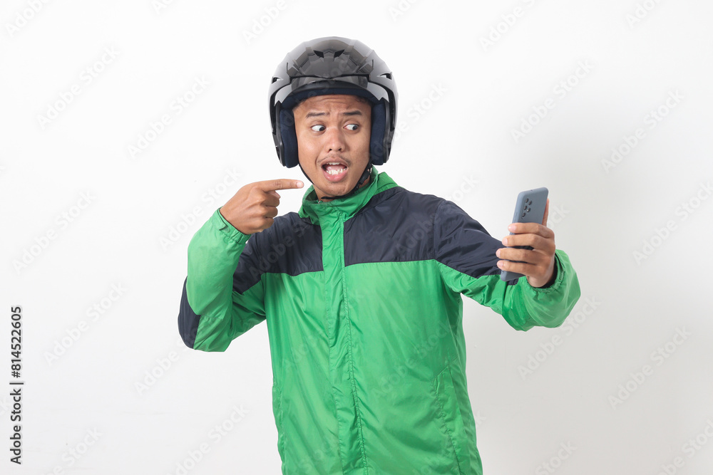 Portrait of Asian online taxi driver wearing green jacket and helmet holding mobile phone while pointing to the side. Isolated image on white background Portrait of Asian online taxi driver wearing green jacket and helmet holding mobile phone while pointing to the side. Isolated image on white background