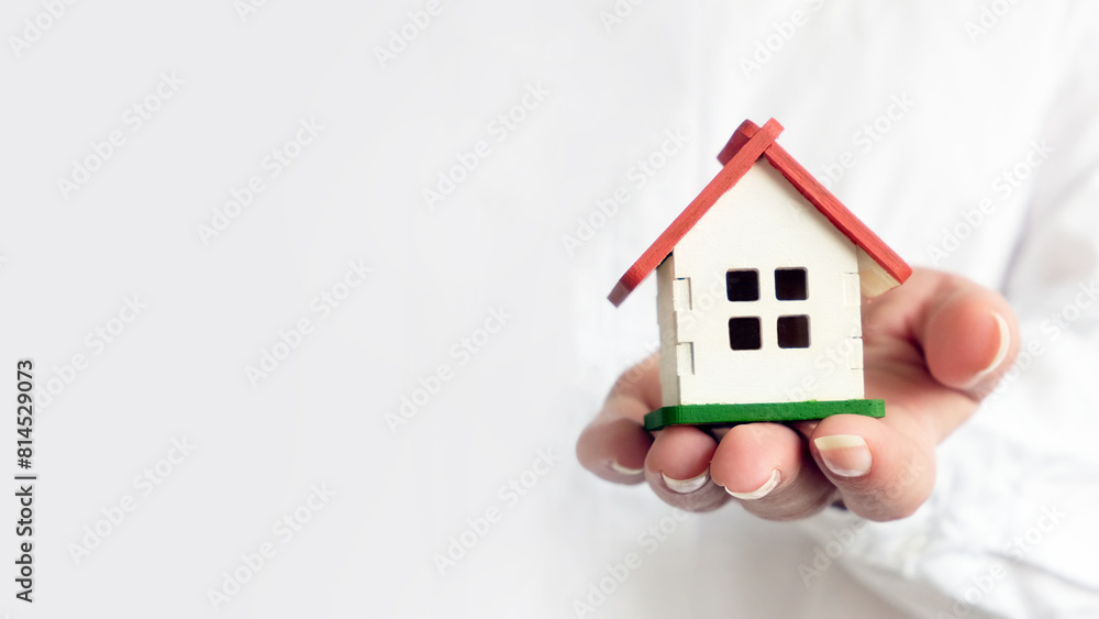 A woman dressed in a white shirt holds a small house in front of her, horizontal banner with a place for text A woman dressed in a white shirt holds a small house in front of her, horizontal banner with a place for text