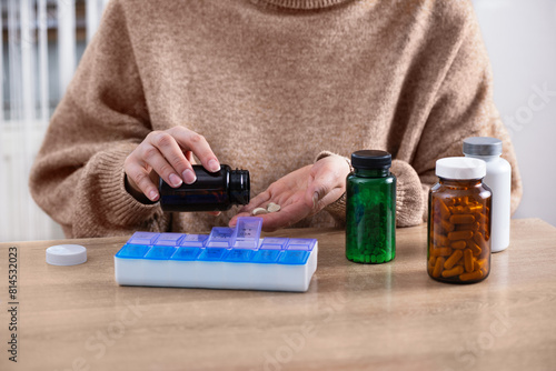 Female putting prescription pills and vitamins in a daily pill box organizer. Sorting nutritional supplements and antibiotics into weekly pills container. © Inna Dodor