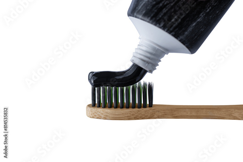Putting charcoal toothpaste on bamboo toothbrush isolated on transparent background. Swatch of black charcoal whitening toothpaste on brush for design.