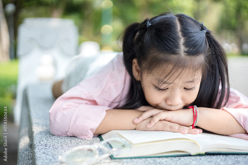 Cute little asian girl reading a book while lying at garden Cute little asian girl reading a book while lying at garden