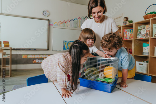 Young female teacher with children playing with hamster in kindergarten