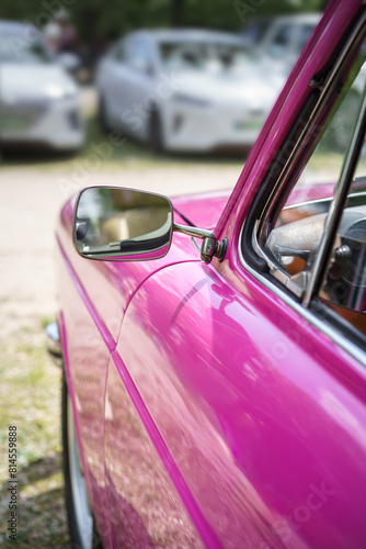 Side view of a vintage car's rear view mirror. Pink colored car. Classic vehicle.