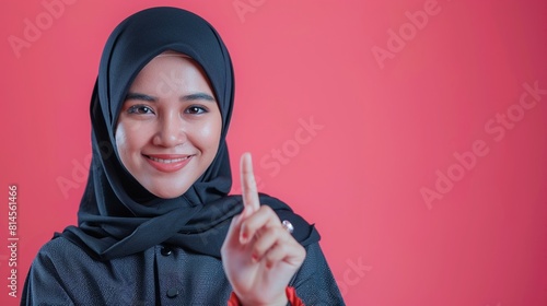 Hijab woman with finger point up on pink background.