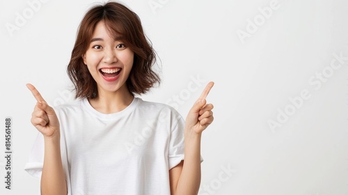 Young asian woman in casual t-shirt, smiling and pointing fingers up at copyspace isolated over white background.