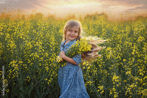 a small beautiful girl in a blue dress with a bouquet of flowers in a rapeseed field is walking for a walk. girl and nature