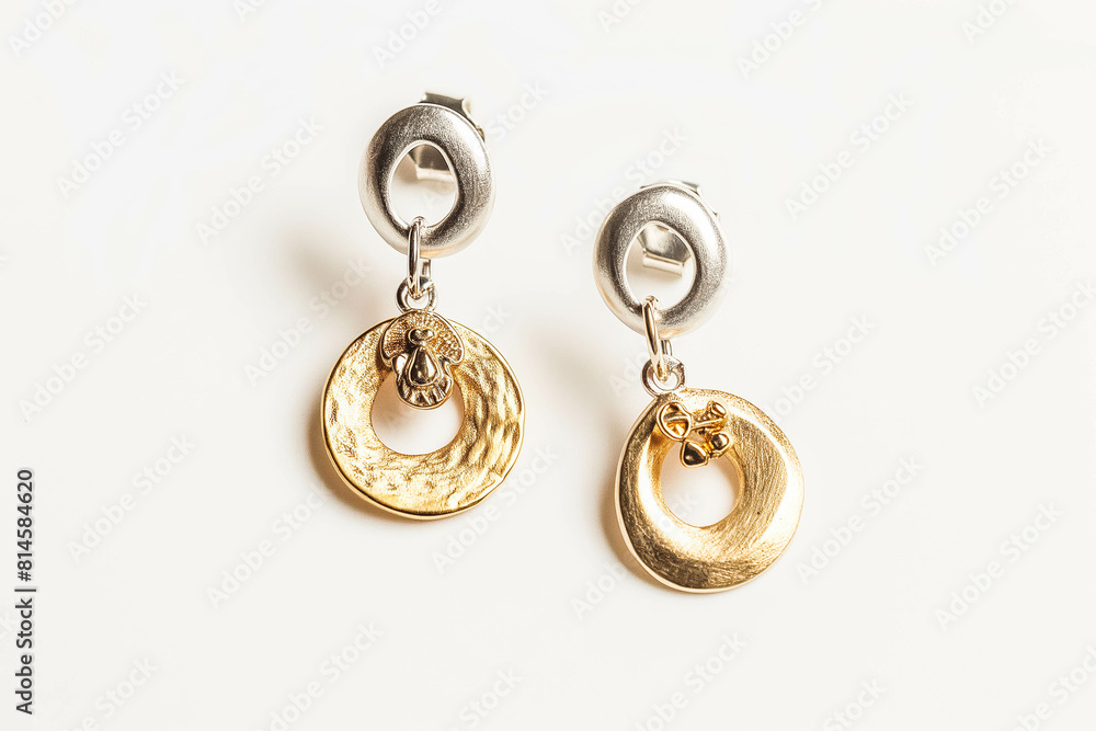 A pair of mismatched earrings, one silver and one gold, with dangling charms, resting on a clean white background. A pair of mismatched earrings, one silver and one gold, with dangling charms, resting on a clean white background.