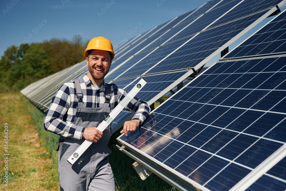 Obraz premium Portrait, holding leveler tool. Engineer with photovoltaic solar panels outdoors at daytime