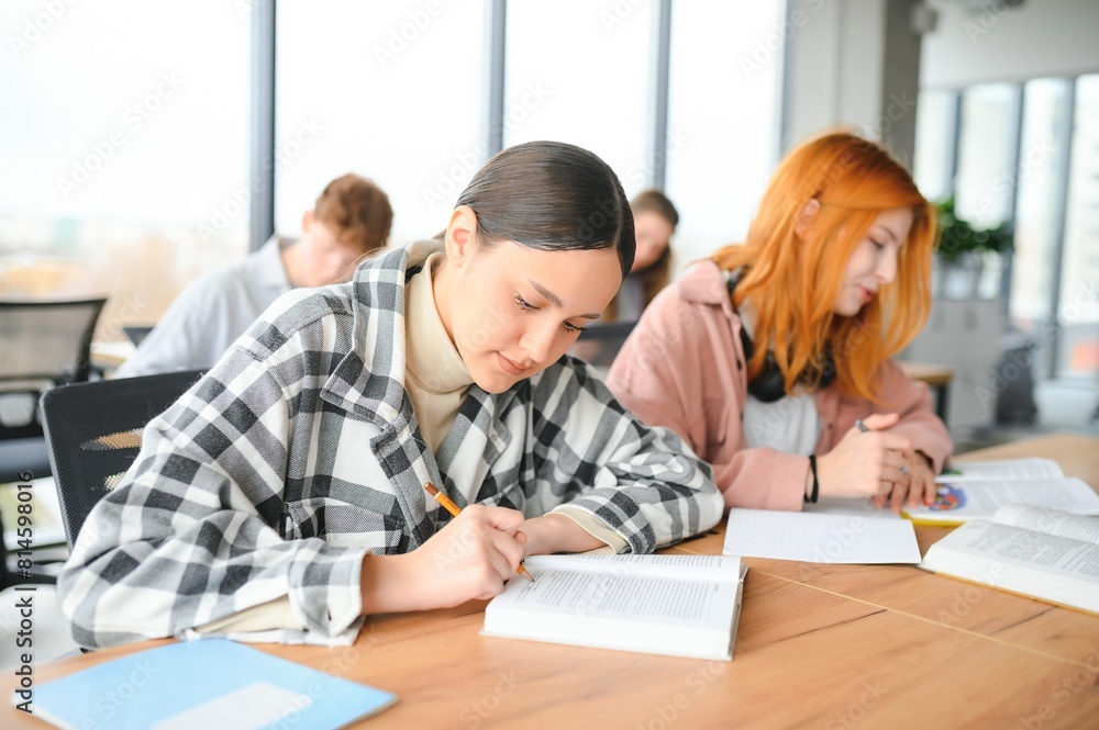 Fototapeta premium students sit at shared desk making notes studying together at university