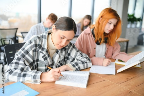 students sit at shared desk making notes studying together at university